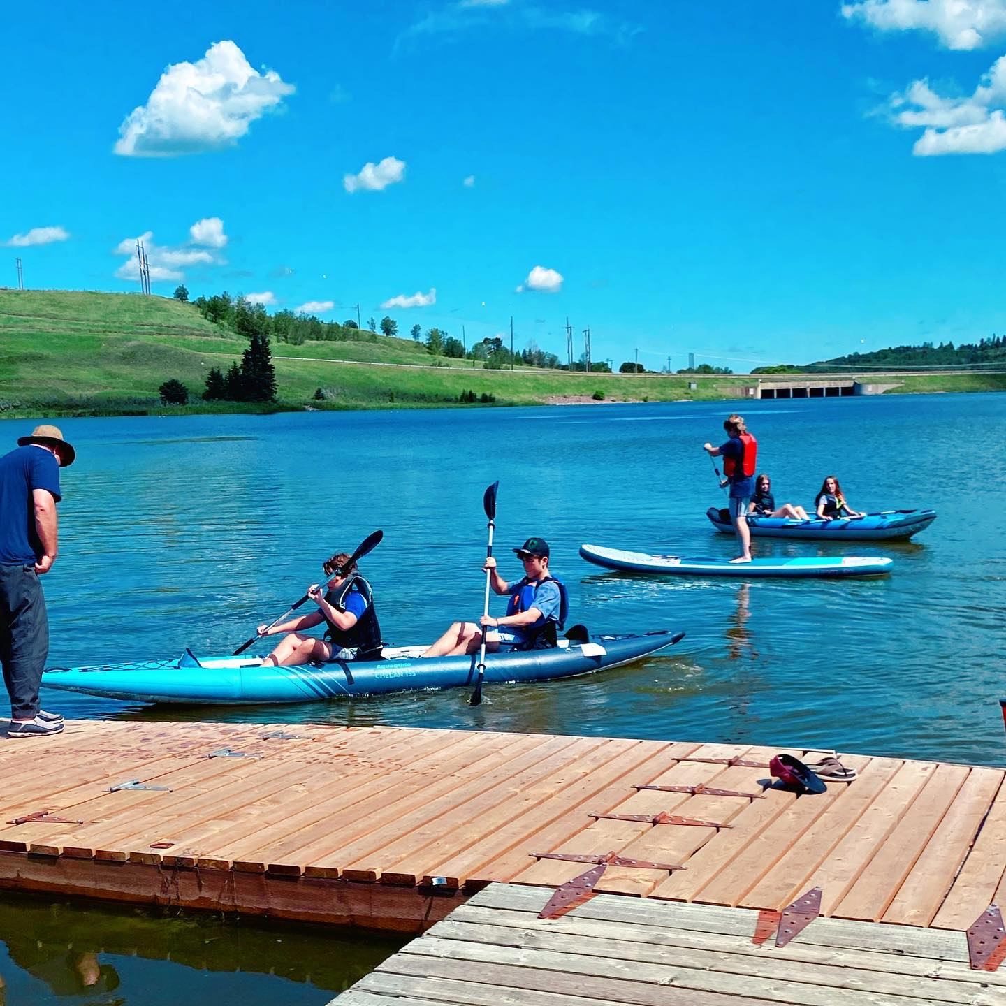 Paddleboarders and kayakers near a wooden dock.