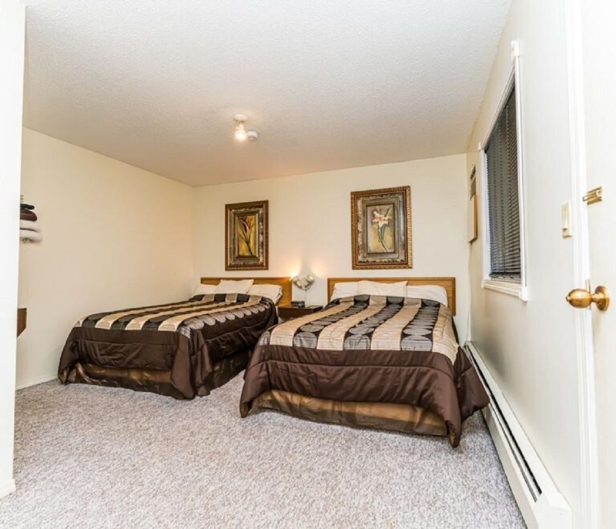 Two neatly made beds in a simple, cozy hotel room with framed art on the wall.