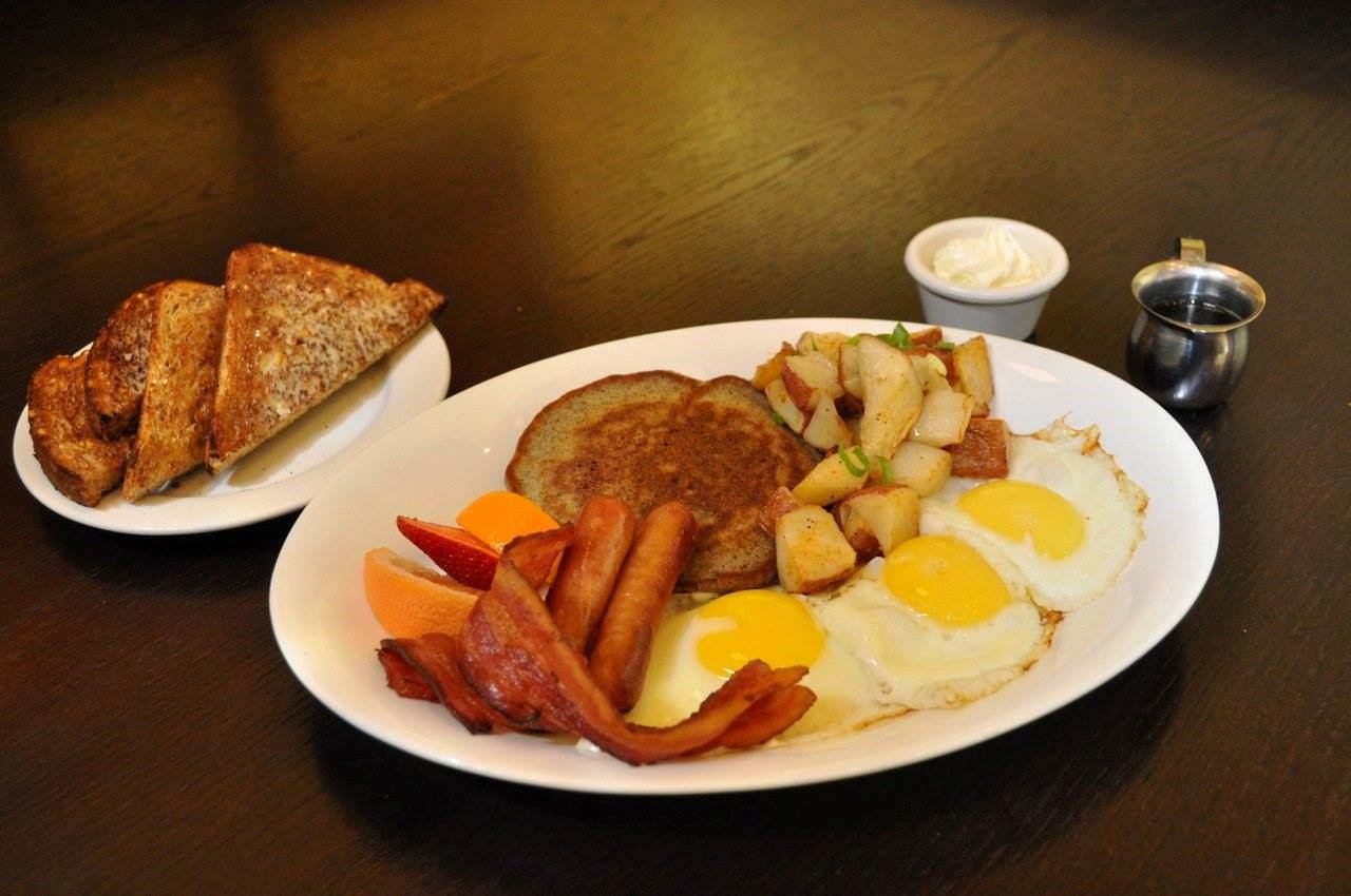 Plate with two fried eggs, toast, potatoes, and sausage on a dark table.