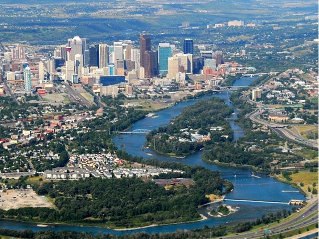 Aerial view of a city with tall buildings, a winding river, and green spaces.