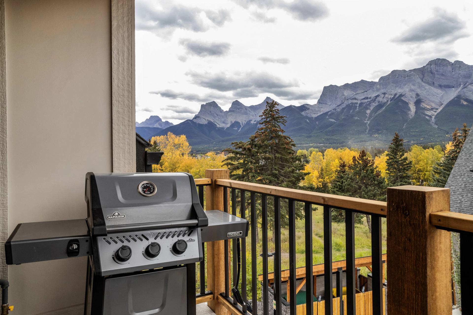 Balcony barbecue grill overlooking forested valley and rugged mountain range under cloudy sky.