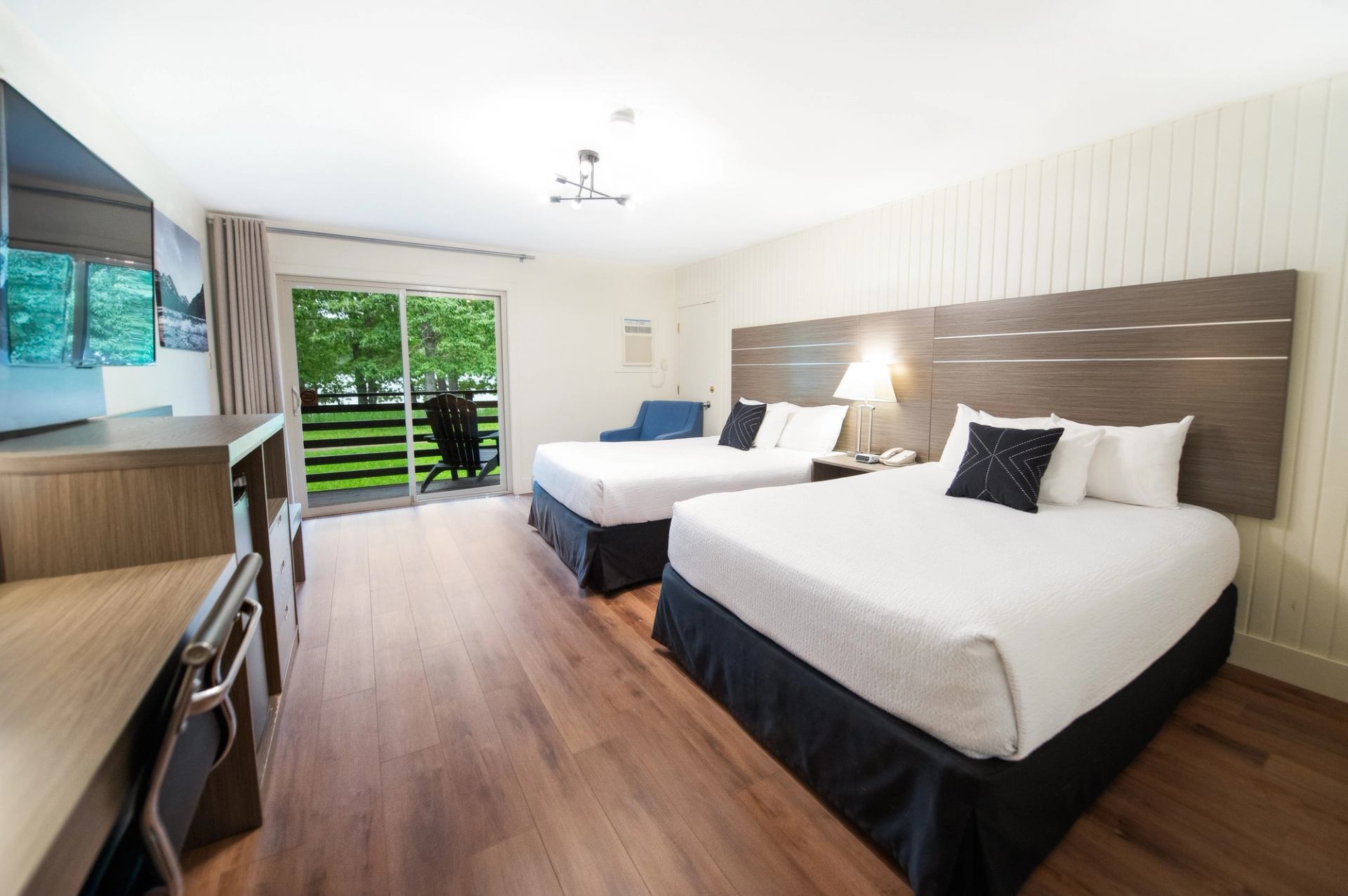 Bright guest room with two beds, desk, seating area, and patio doors overlooking greenery.