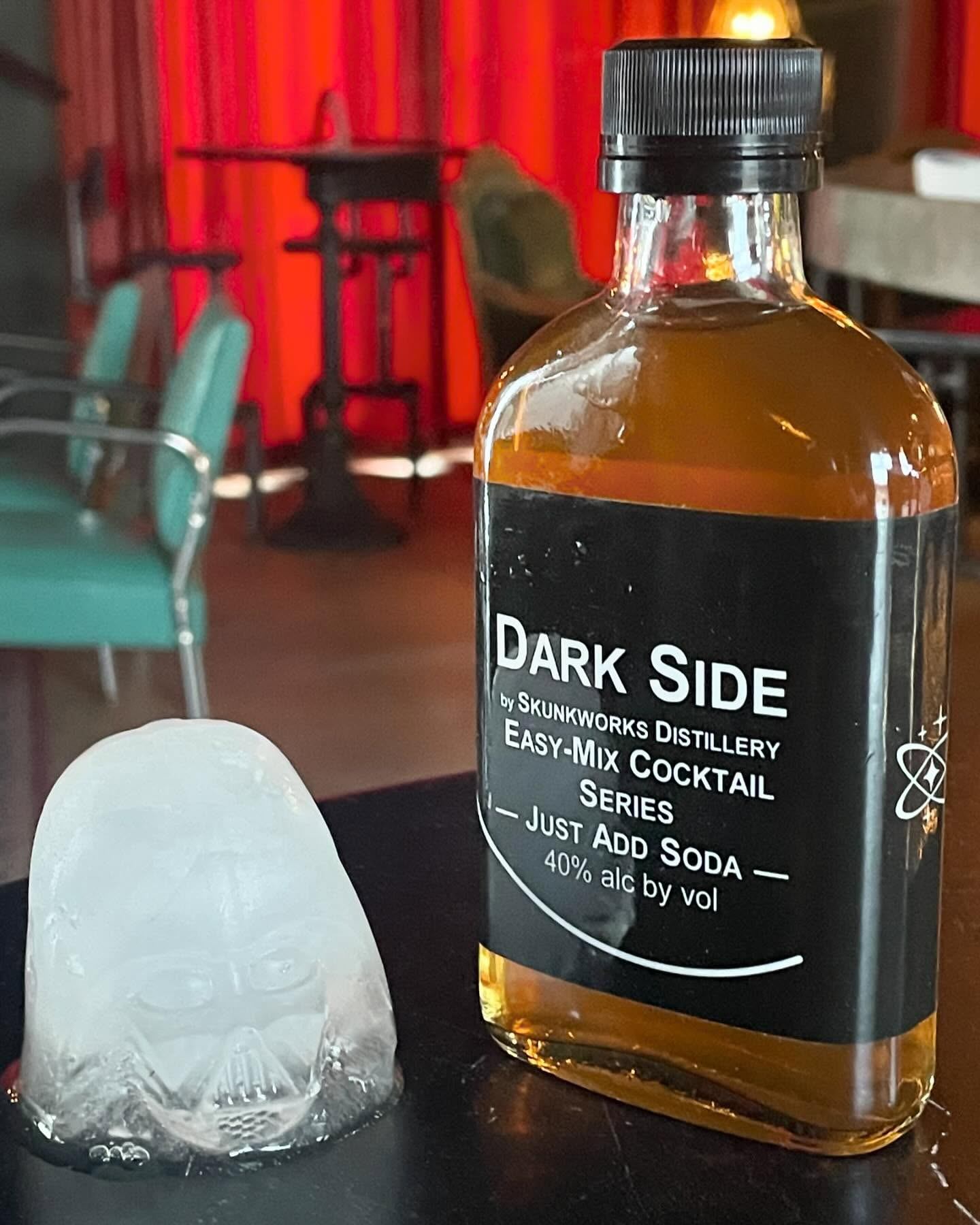 Dark Side easy-mix cocktail bottle beside a clear ice cube inside the distillery.