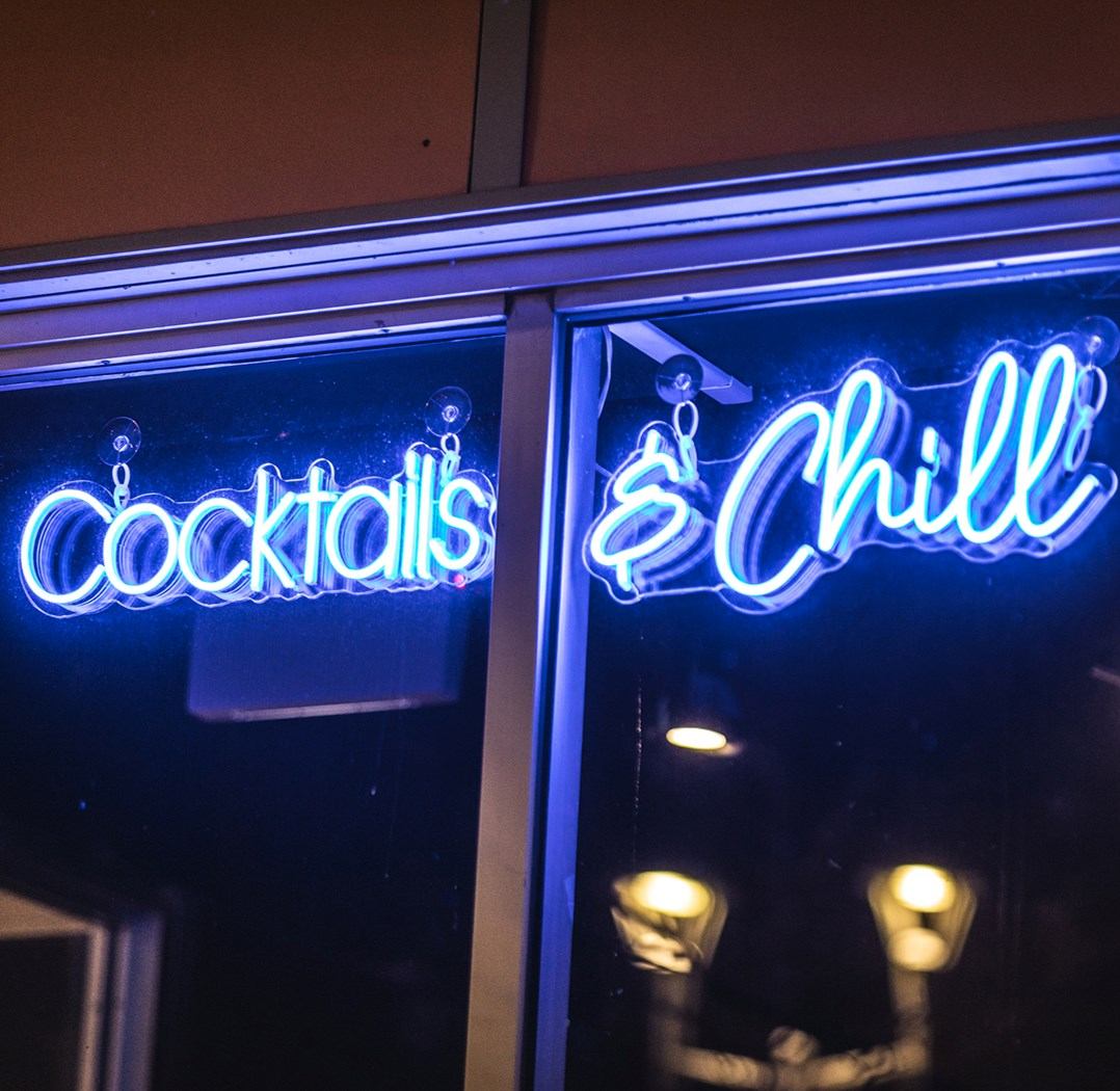 Neon sign inside a bar reading “Cocktails” and “Chill” with cocktail icons.