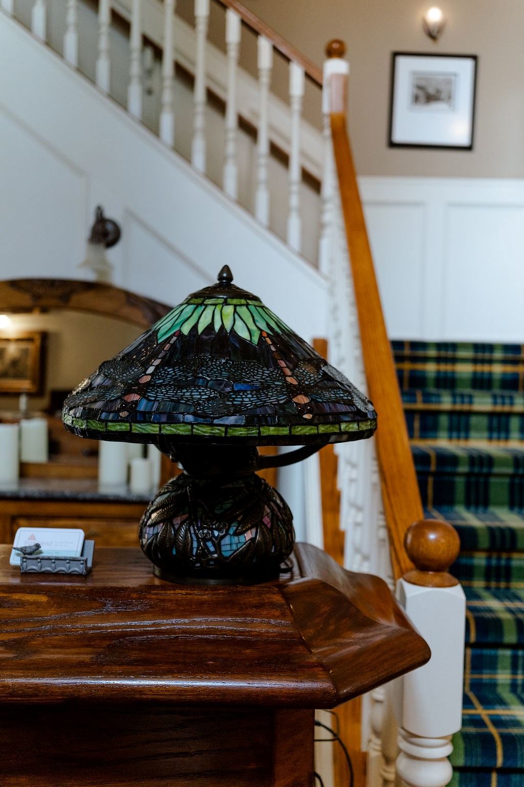 Decorative stained-glass lamp on wooden table inside a motel lobby with stair railing and plaid chai.