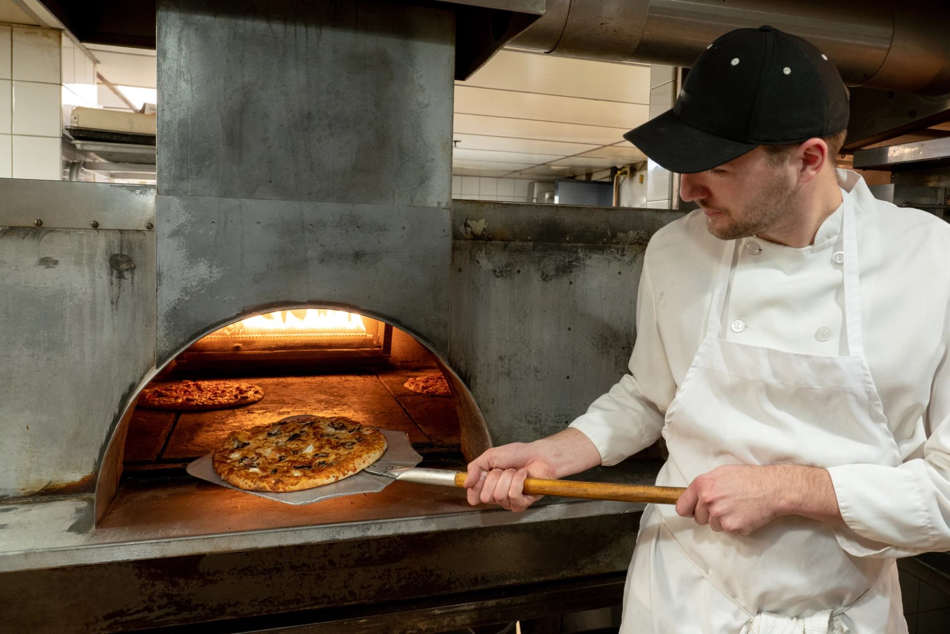 Chef placing pizza in wood-fired oven with open flame.