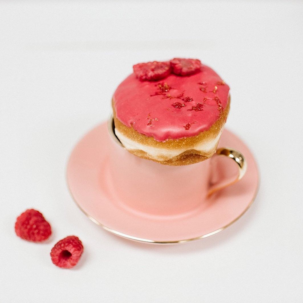Pink glazed donut with raspberries on a pink cup and saucer