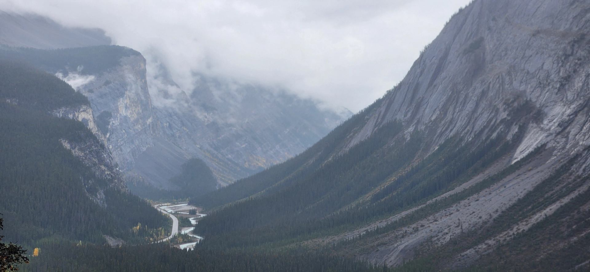 Foggy mountain valley with steep rocky slopes and winding river below.