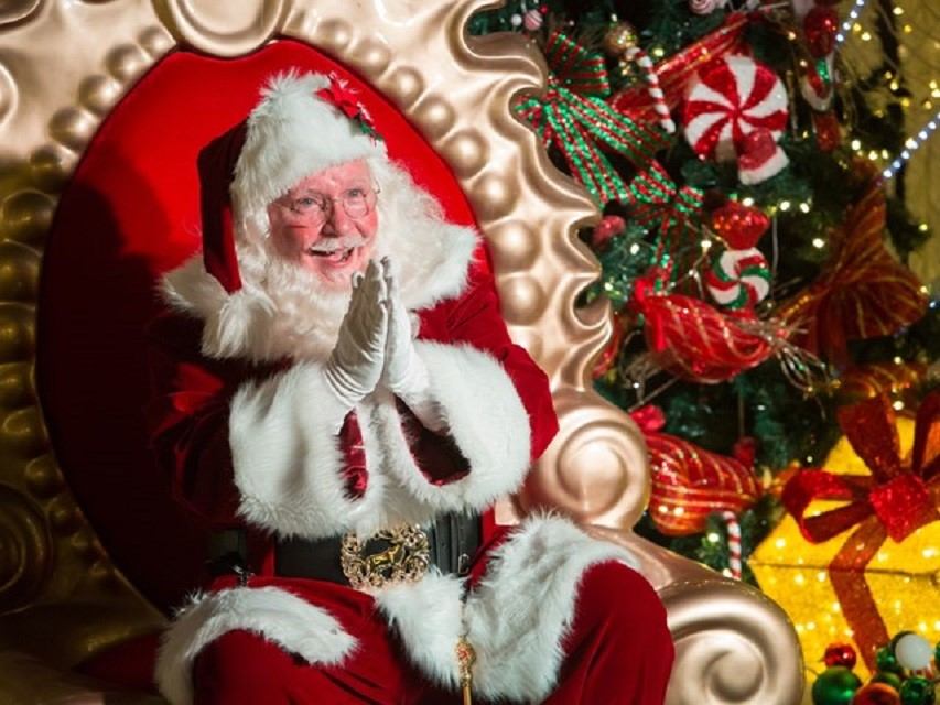 Santa Claus seated in a festive chair beside a decorated Christmas tree at Glow Festival.