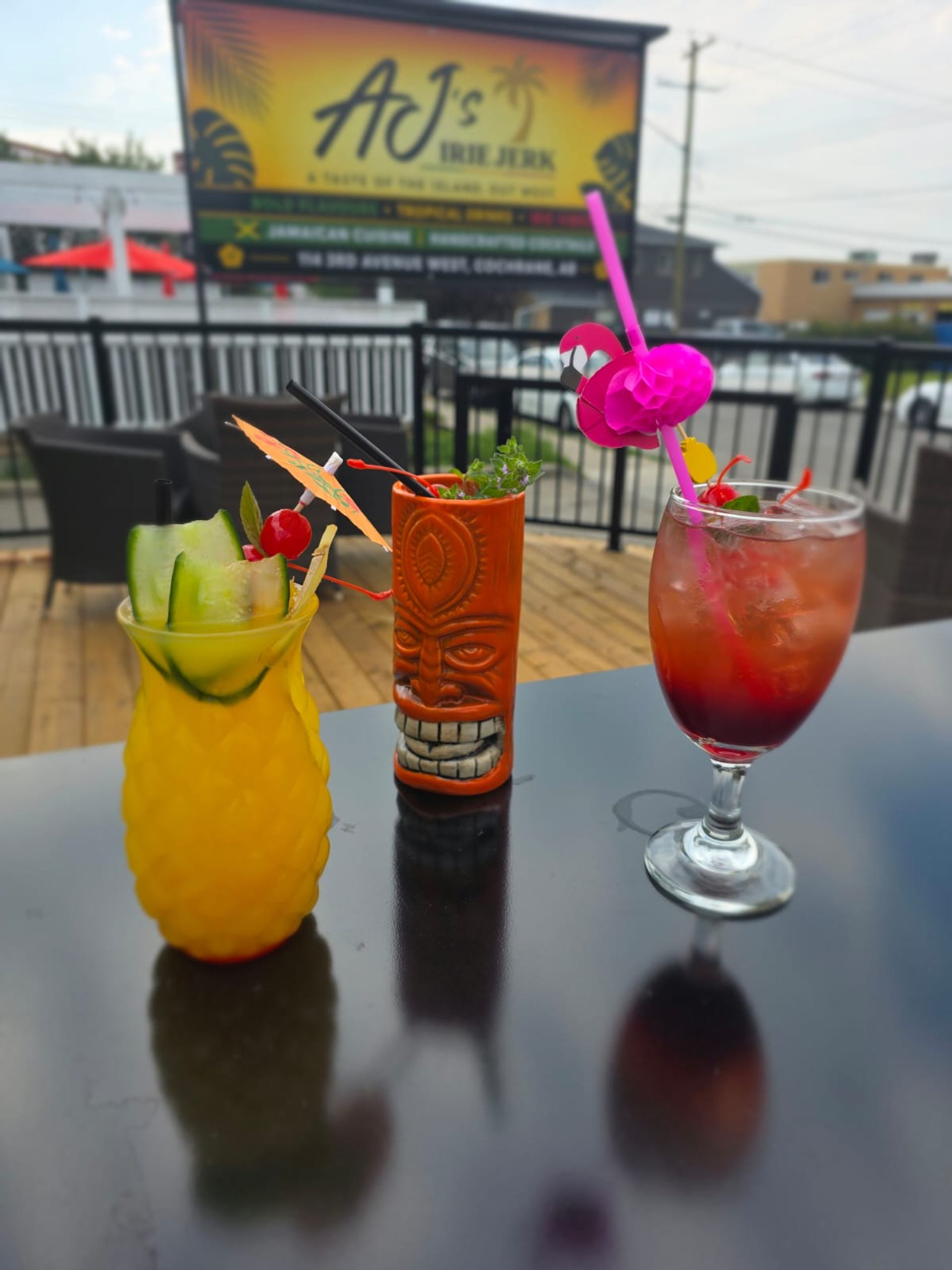Colourful tropical drinks with fruit garnishes sit on an outdoor table at AJ's Tiki Juke.