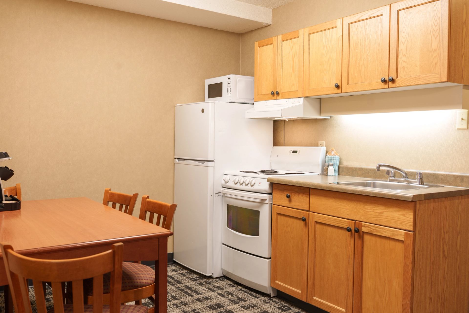 Small kitchen with wooden cabinets, white appliances and dining table with chairs.
