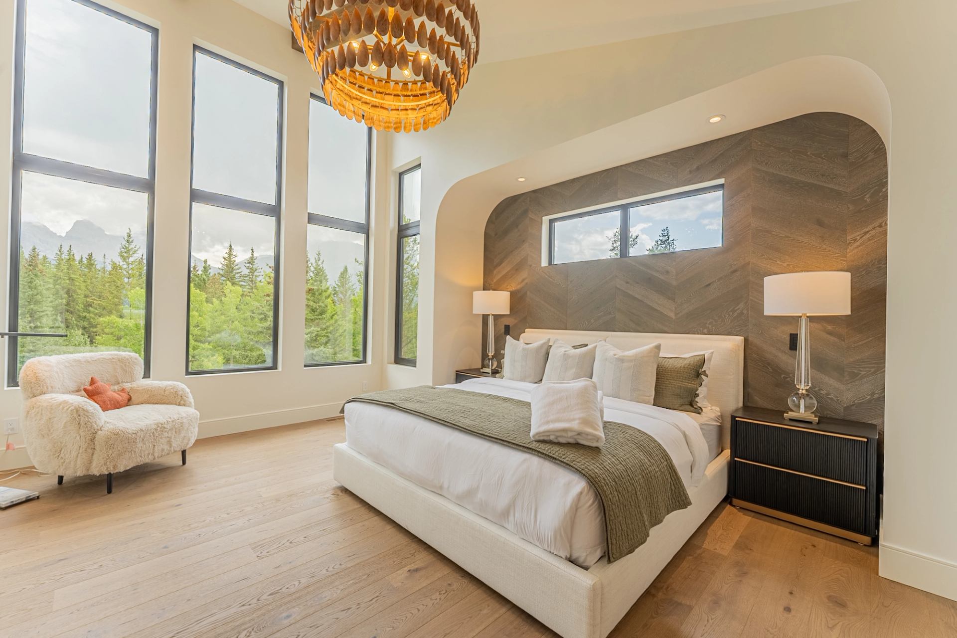 Bedroom with upholstered bed, wood feature wall, large windows and a shaggy armchair.