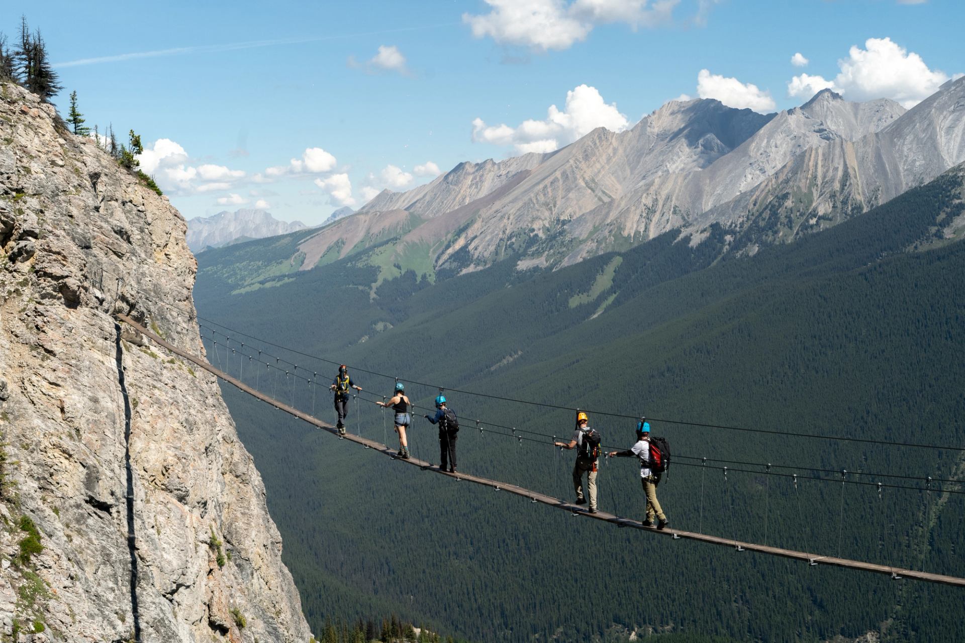 Adventurers crossing a high suspension bridge in the mountains.