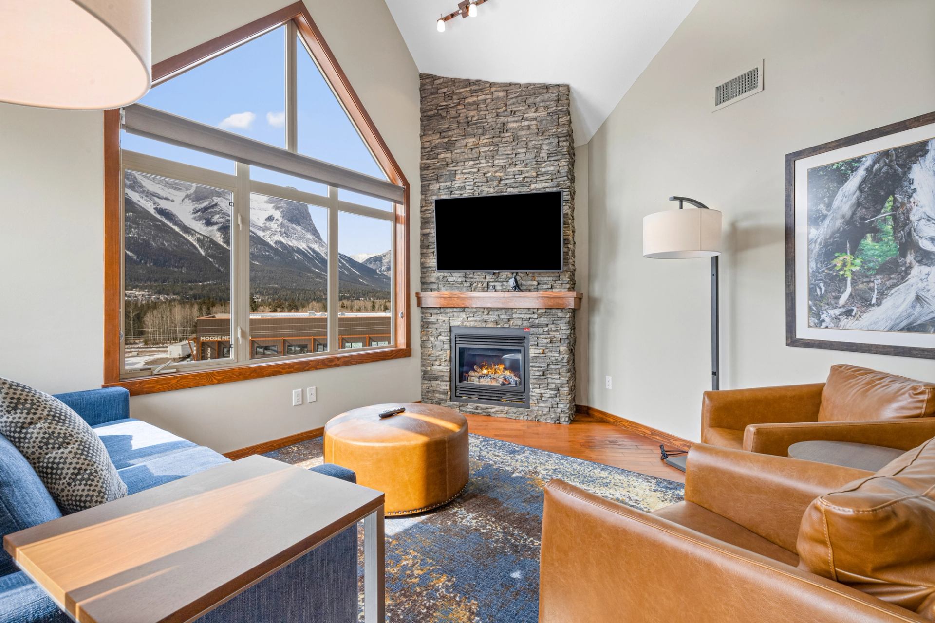 Living room with stone fireplace, leather chairs and large windows overlooking mountains.
