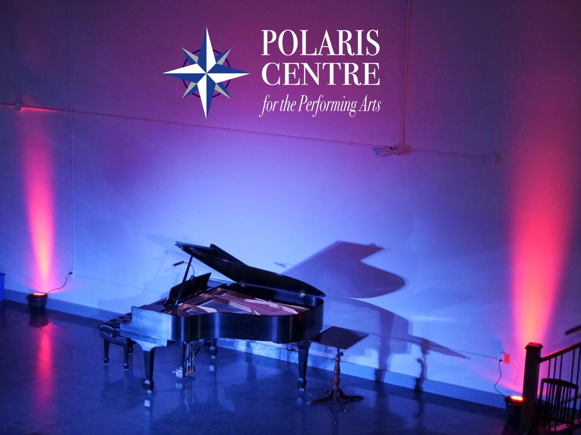 Grand piano under colorful stage lights with Polaris Centre logo in the background.
