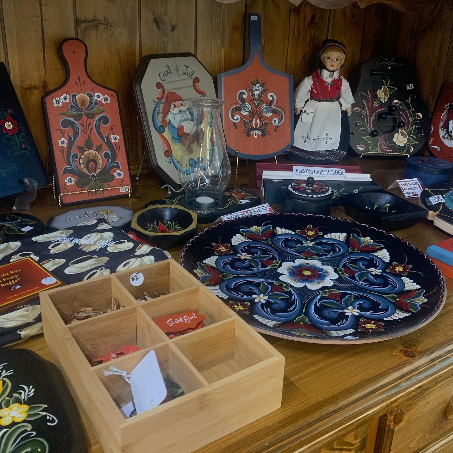 Painted wooden crafts, trays, and doll in traditional attire on display.