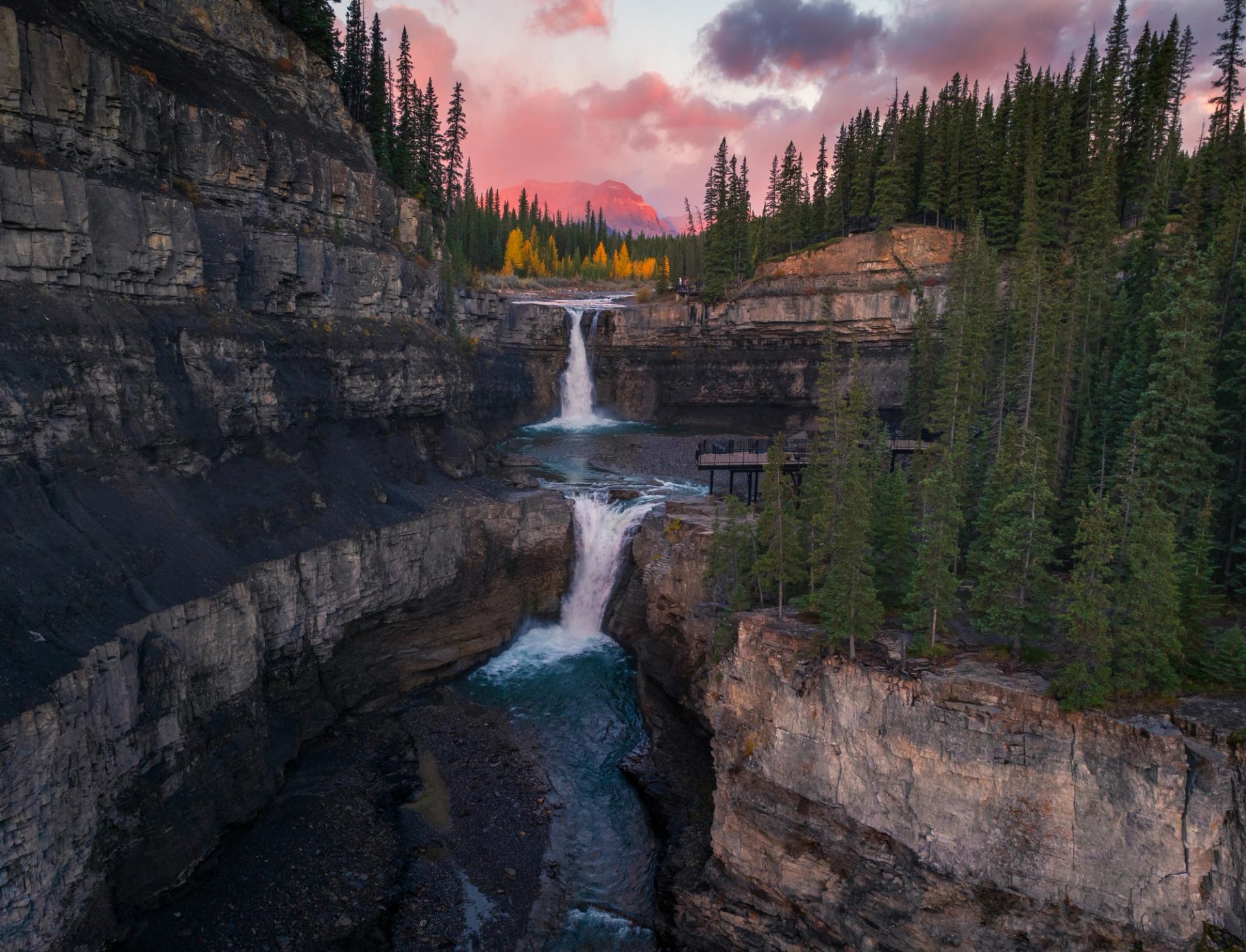 Crescent Falls cascades through rugged cliffs surrounded by dense forest at sunset.