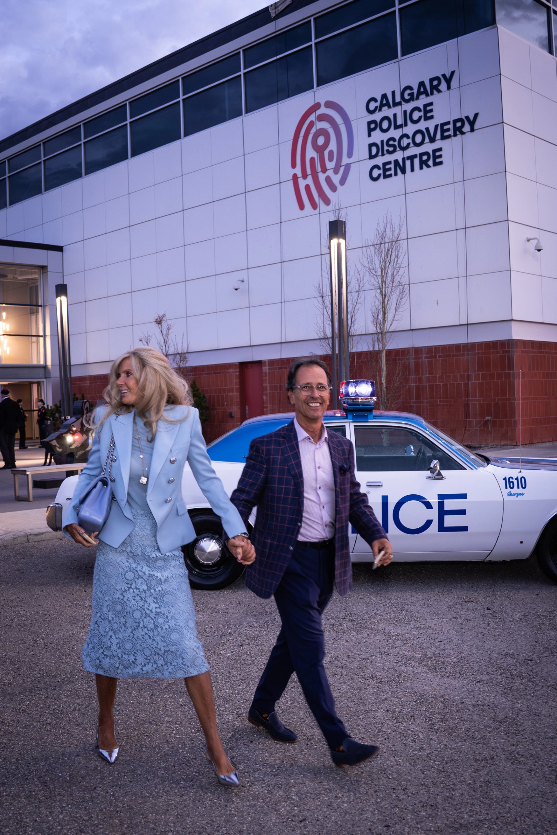 Pair walks past a vintage police car outside Calgary Police Discovery Centre.