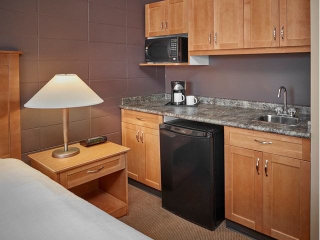 Hotel room kitchenette with cabinets, microwave, mini-fridge, sink, coffee maker, lamp.