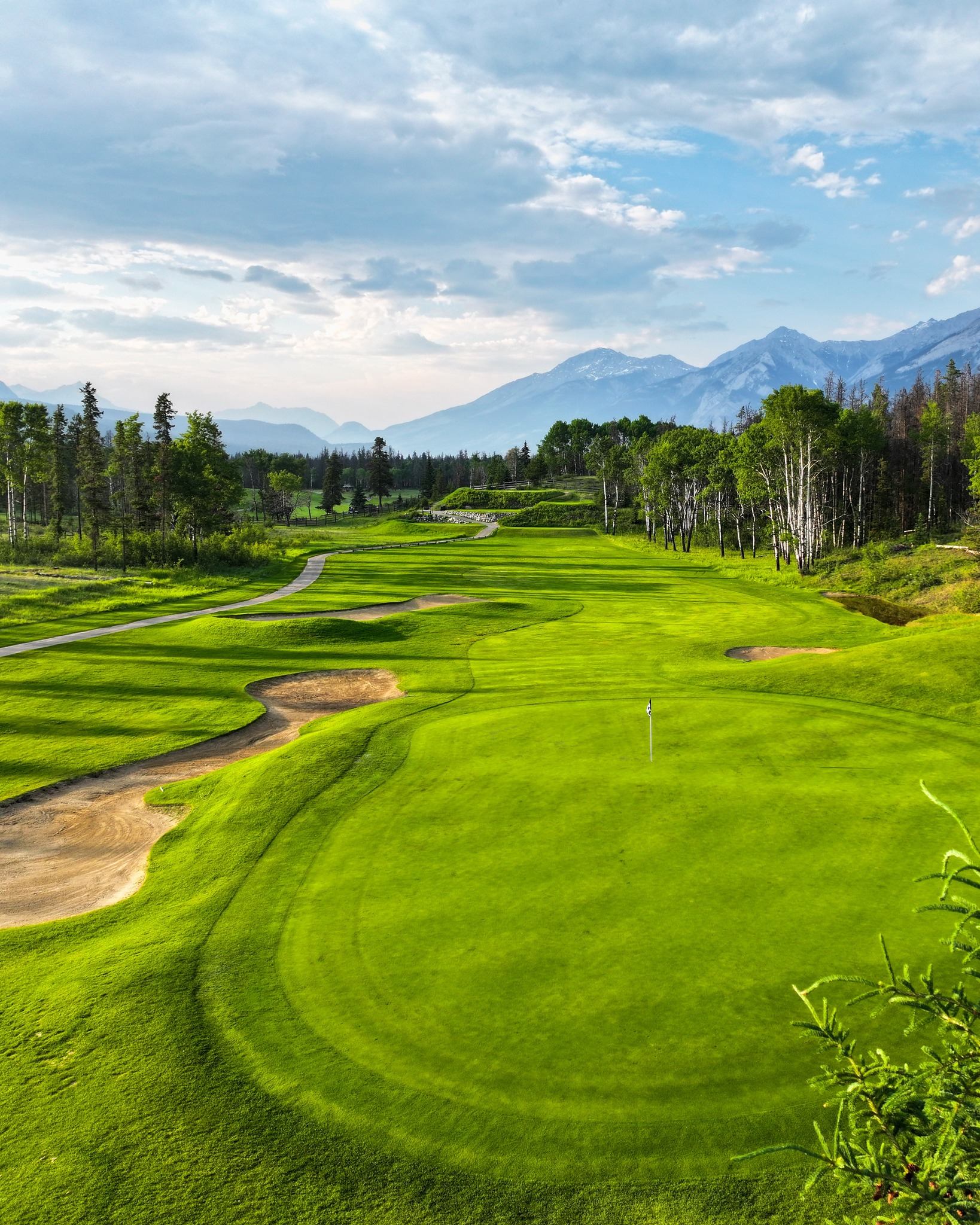 Golf course fairway with sand traps, flag, trees and mountains in Jasper National Park landscape.