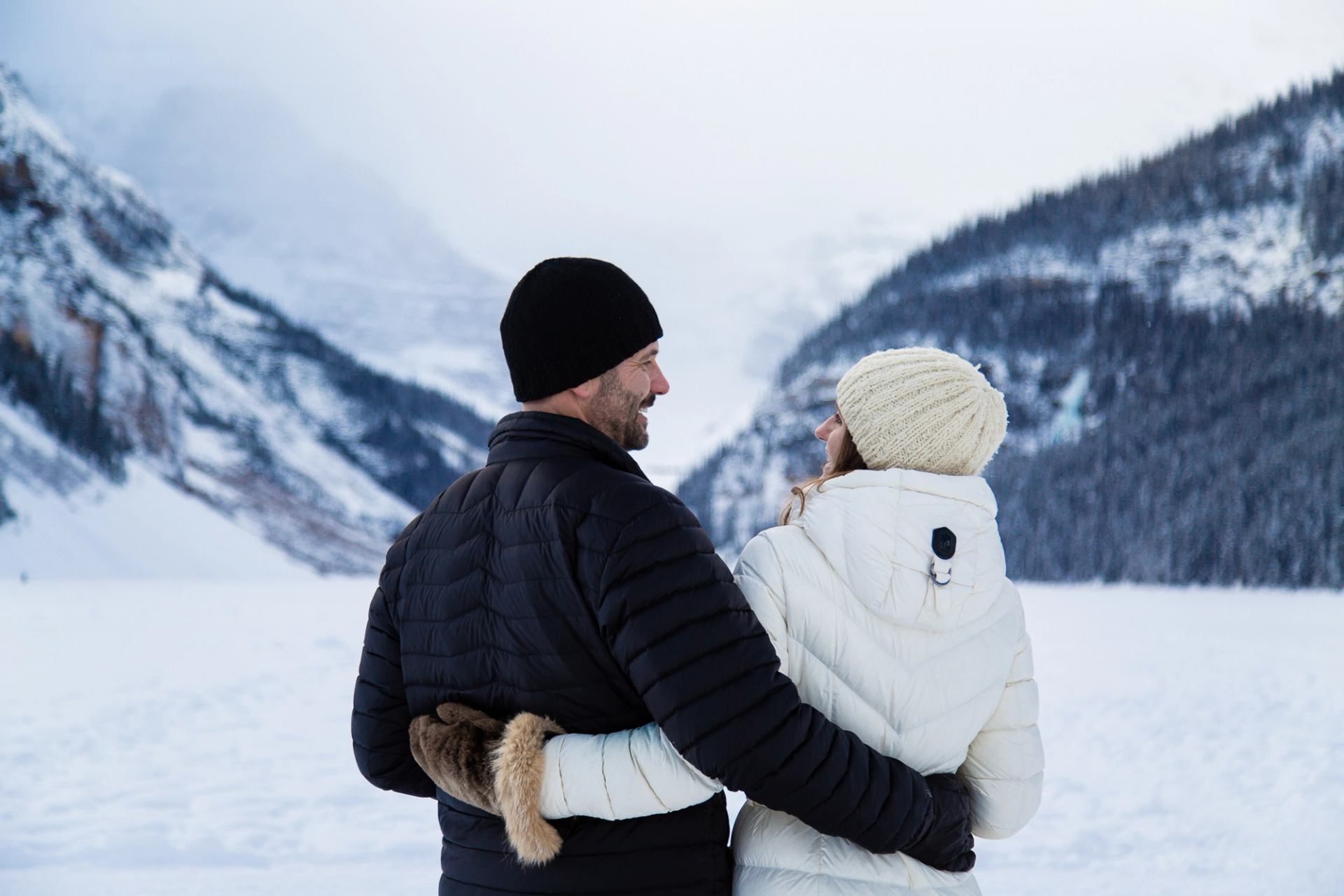 Two people standing close together in a snowy mountain landscape.