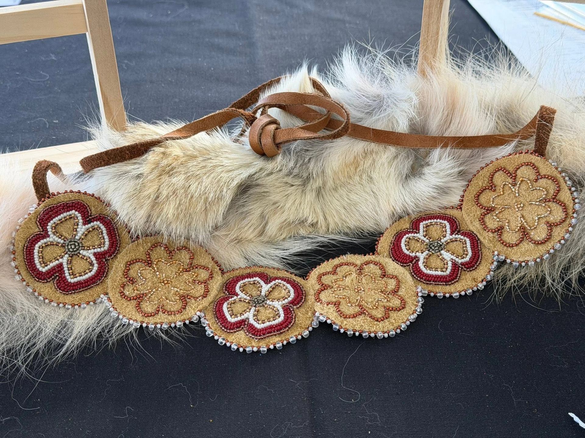 Beaded floral belt with circular designs resting on light fur and dark fabric.
