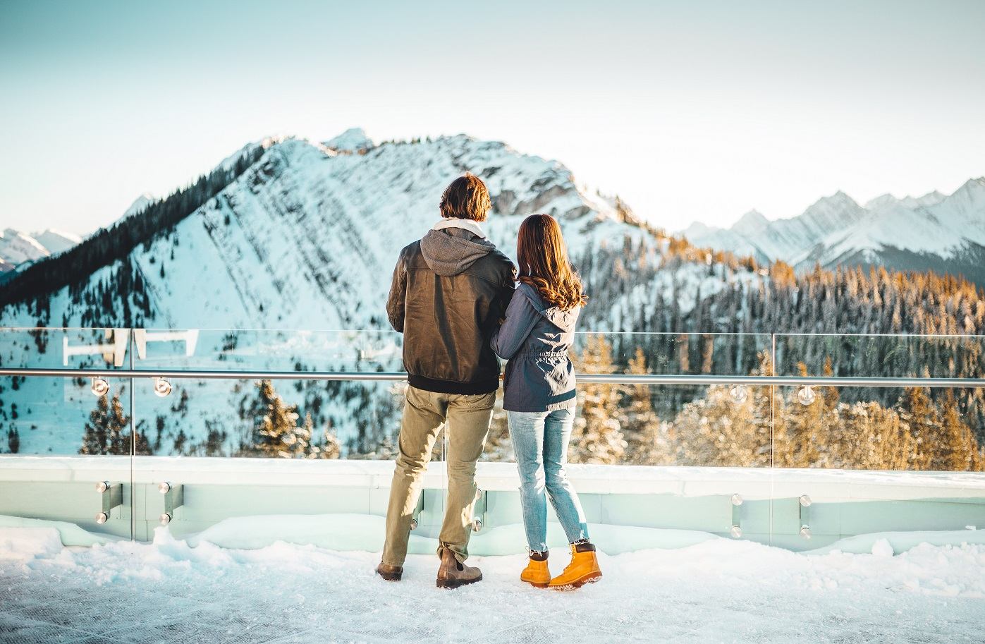Two people admire snowy mountain views from a winter lookout in Banff.
