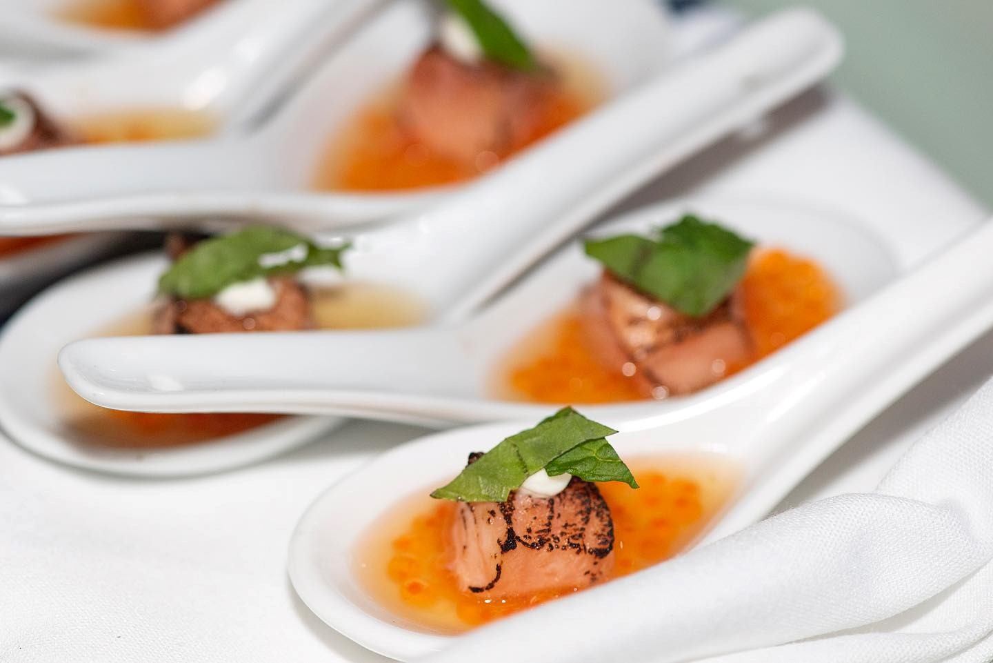 Close-up of gourmet appetizers served in white ceramic spoons with vibrant garnishes.