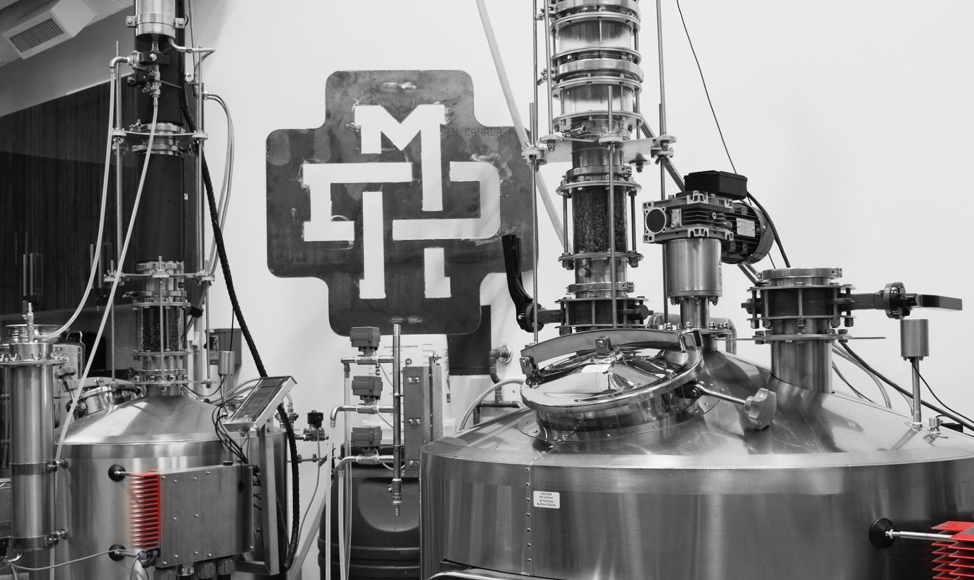 Stainless steel distillery equipment with large “MD” logo plate in grey background.