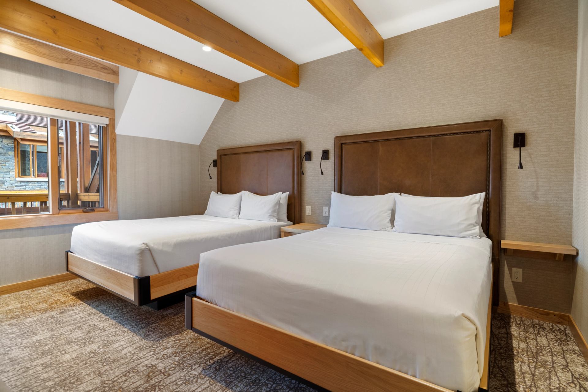 Two queen beds in a room with wood beams on the ceiling and a window