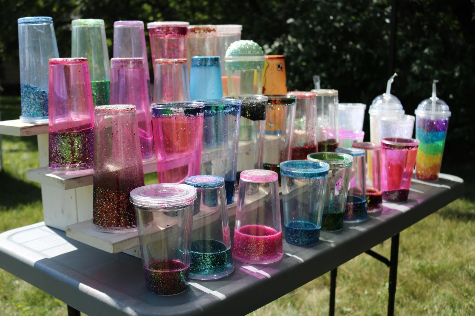 A table filled with colourful glitter tumblers displayed outdoors.