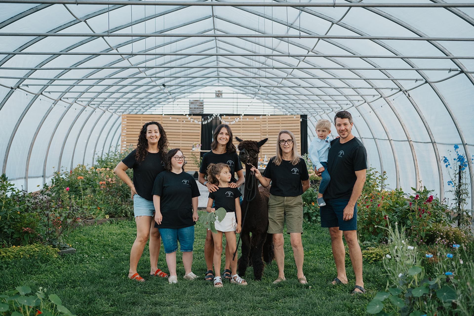 Group standing in a greenhouse with flowers and an alpaca at Blooms on 7 Flower Farm.