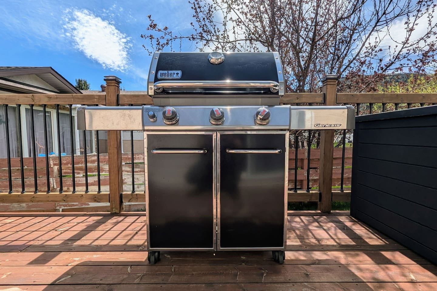 A black and silver Weber gas grill on a wooden deck next to a black storage box.