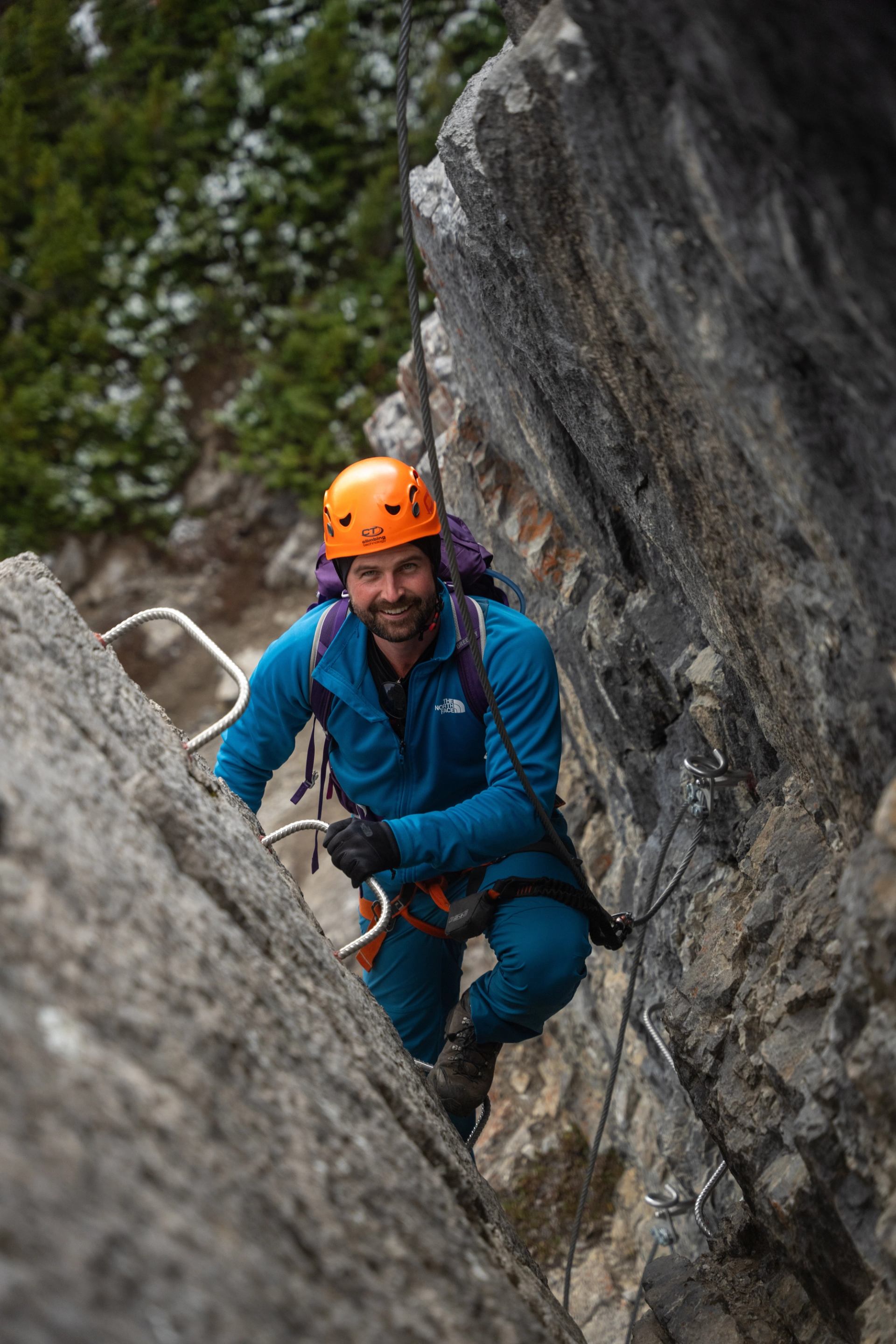 Climber in helmet and harness ascending a narrow rock crevice