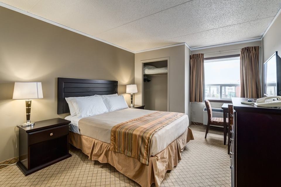 Hotel room with queen bed, nightstands, lamps, desk, chair, and window with city view.