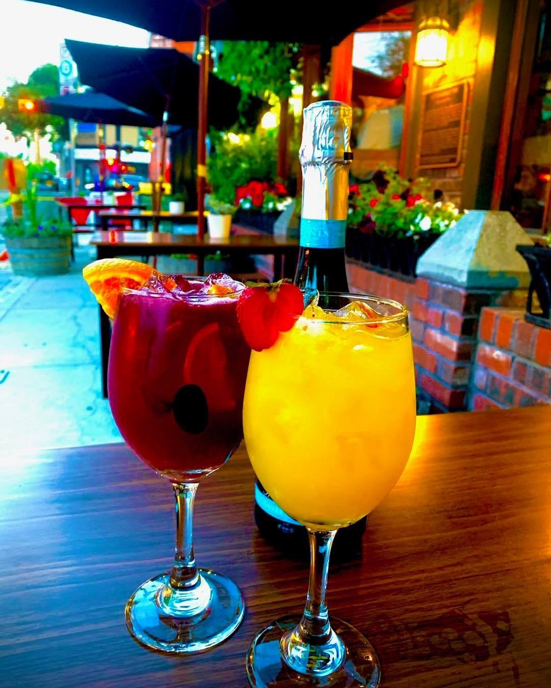 Red and yellow cocktails with fruit garnish on patio table at Kensington Pub.