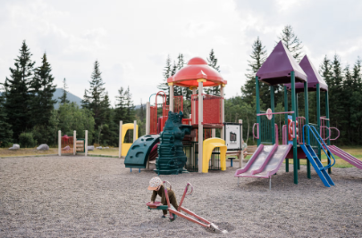 Playground with colourful slides and climbing structures surrounded by trees and distant hills.