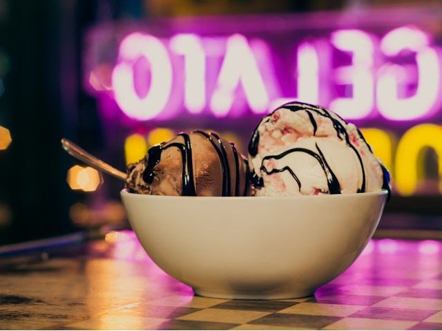 Chocolate and strawberry swirl ice cream scoops with syrup in a white bowl.