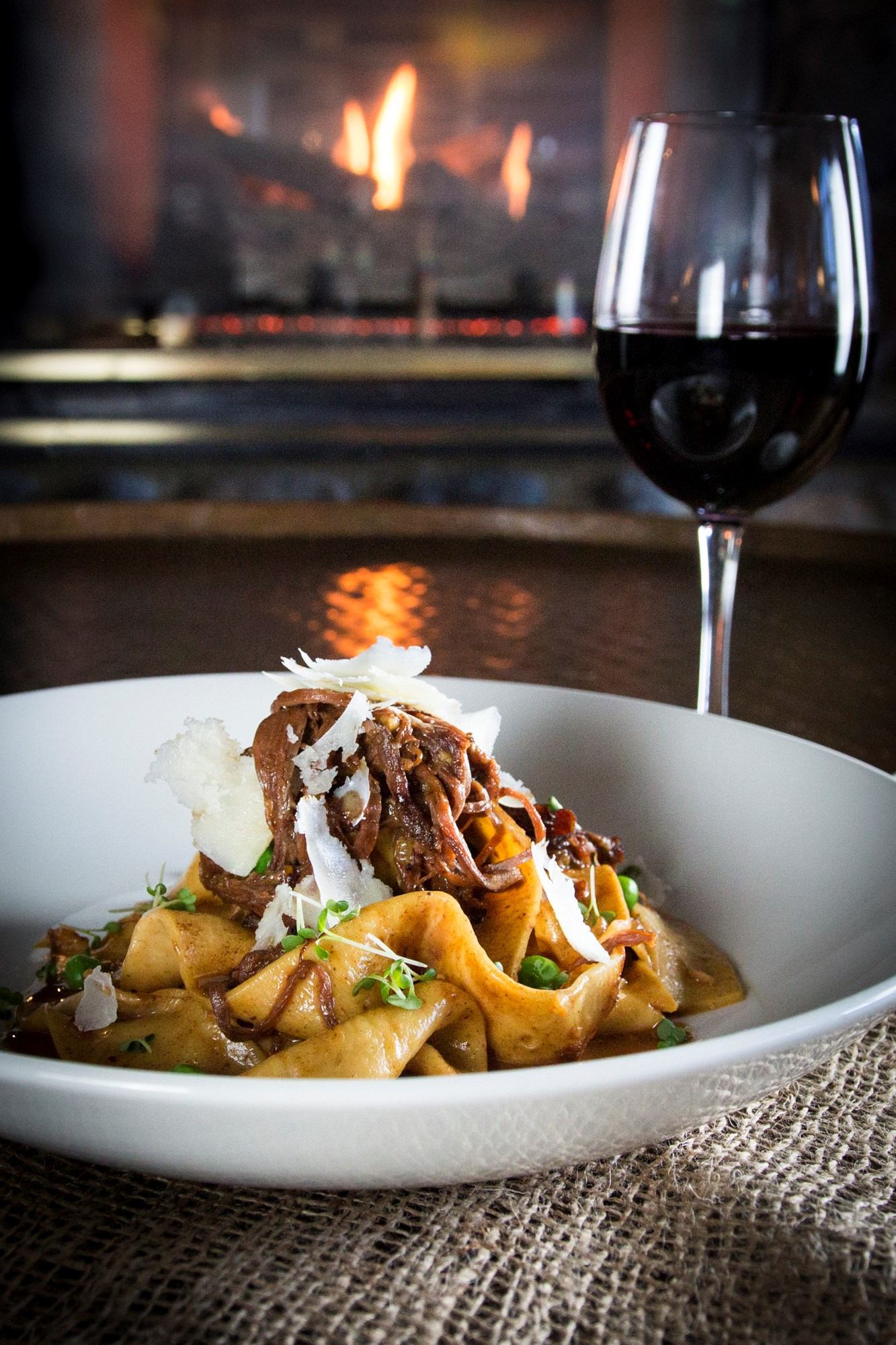 Pasta with meat sauce, cheese, and wine by a cozy fireplace.