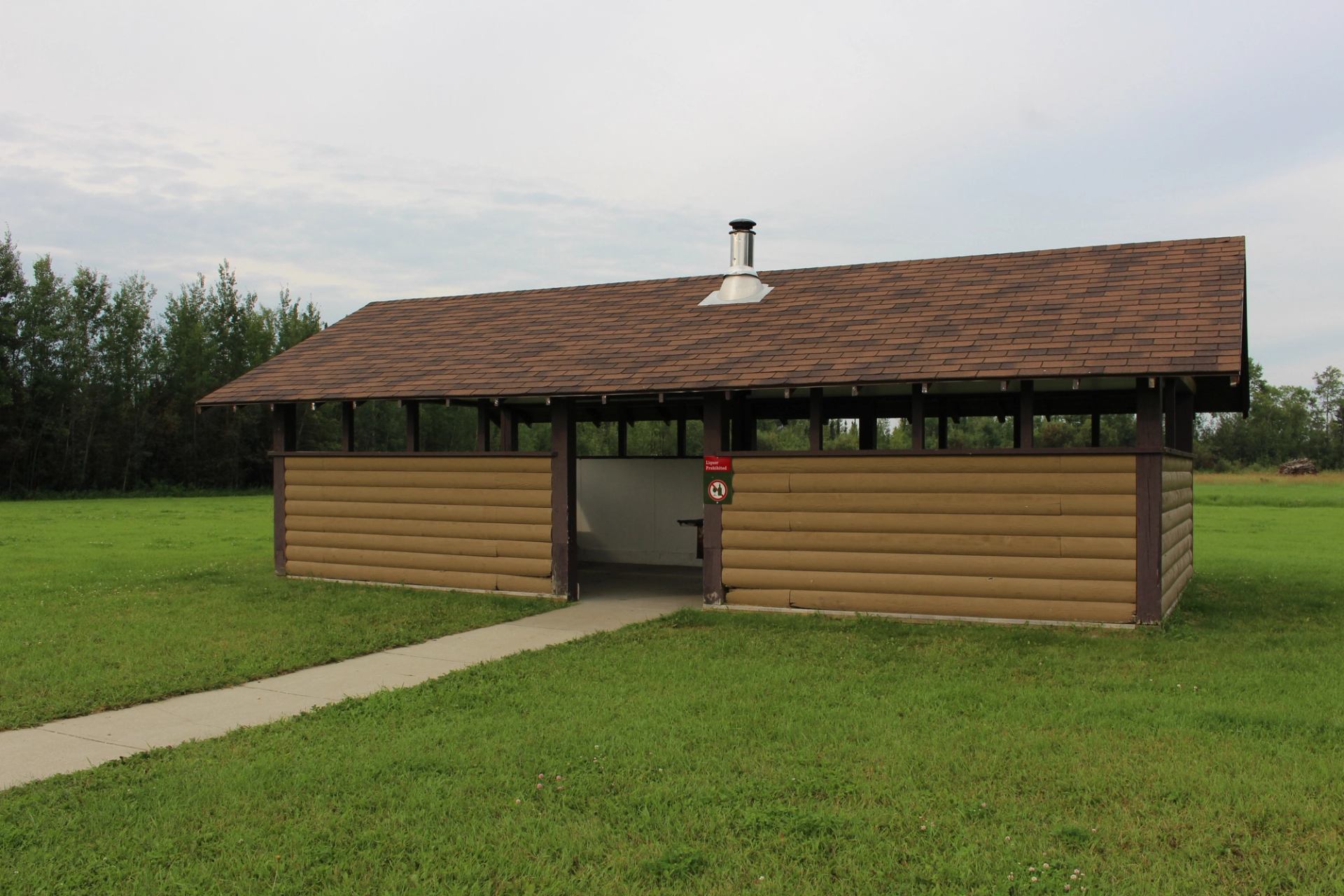 Small brown-roofed shelter or restroom in grassy park area with pathway.