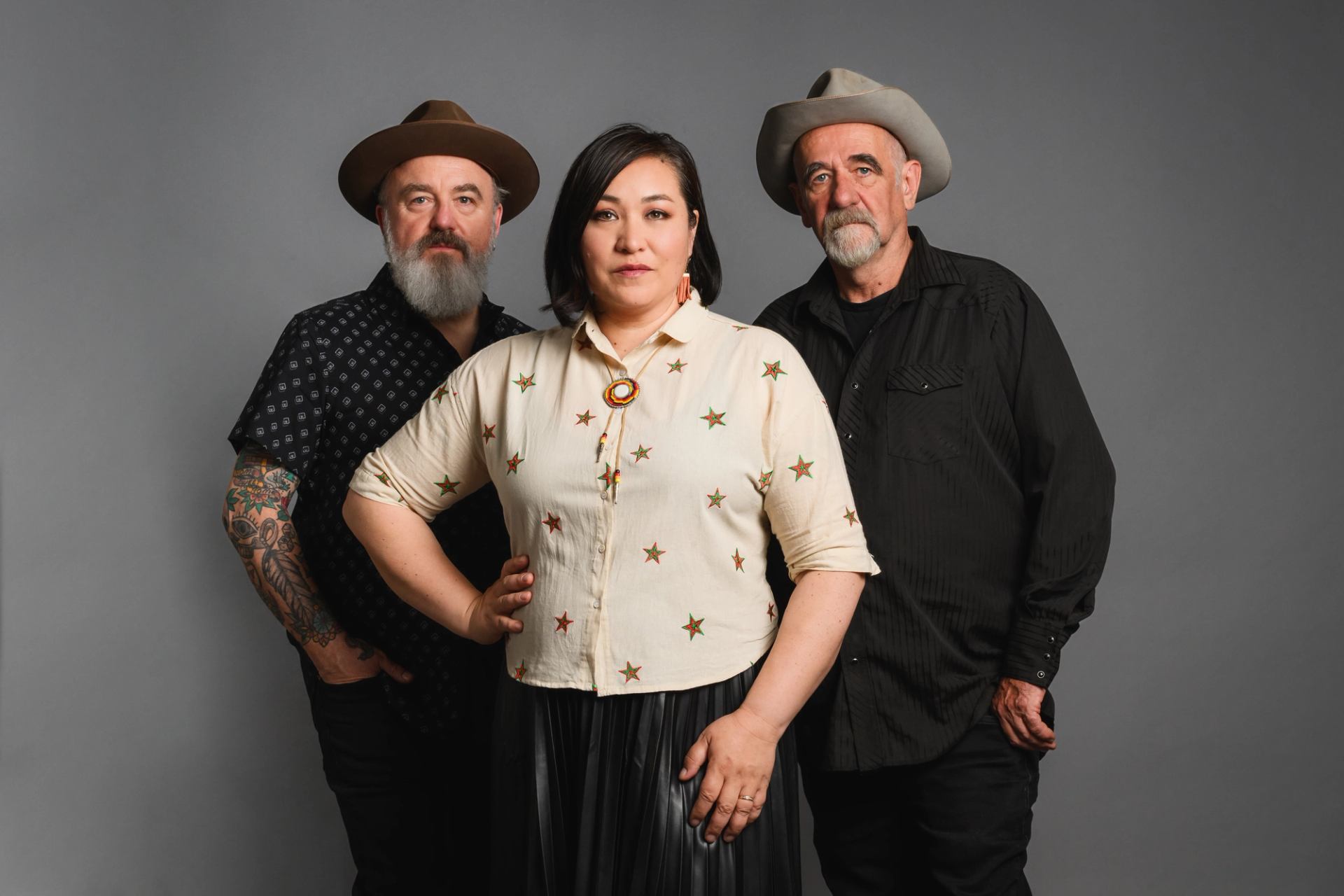 Three people in hats and patterned shirts stand together against a plain grey background.