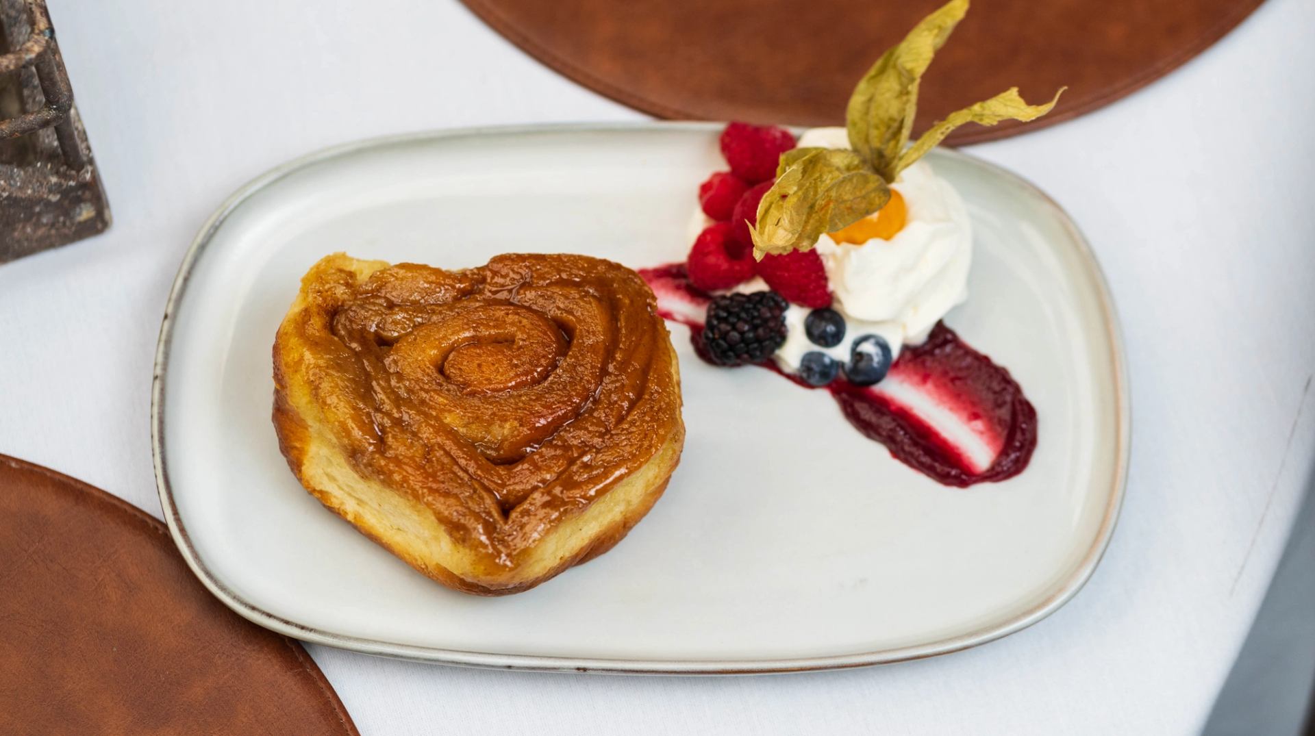 Heart-shaped pastry on plate with whipped cream, berries and berry sauce.