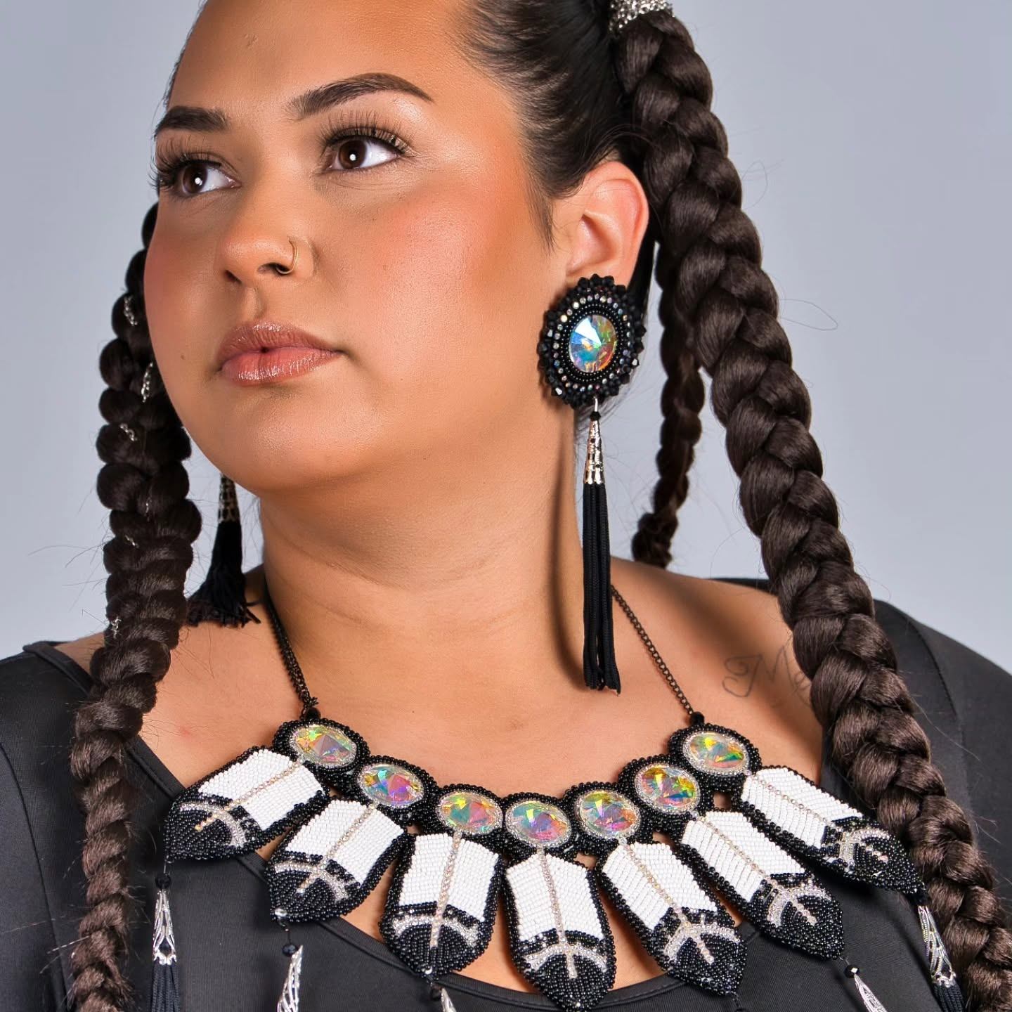 Person with long braids wearing large beaded earrings and feather-patterned beaded necklace.