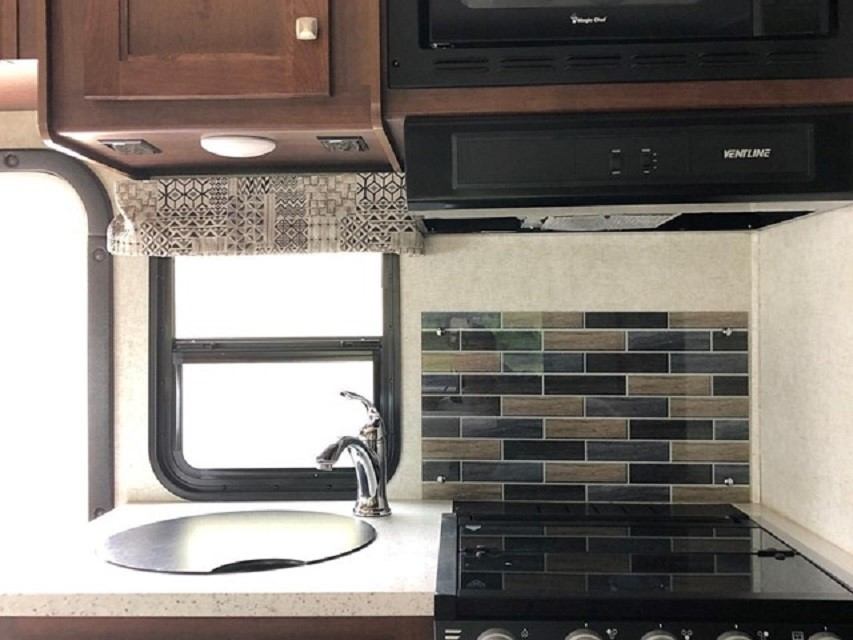 RV kitchenette with sink, tiled backsplash, and built-in cooktop with hood.