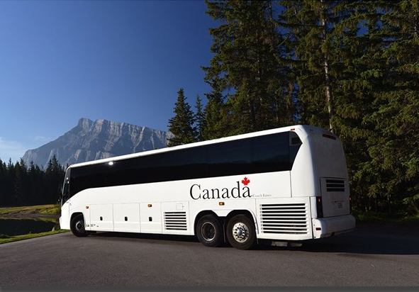 Canada Coach Lines bus on road beside trees with mountain backdrop.