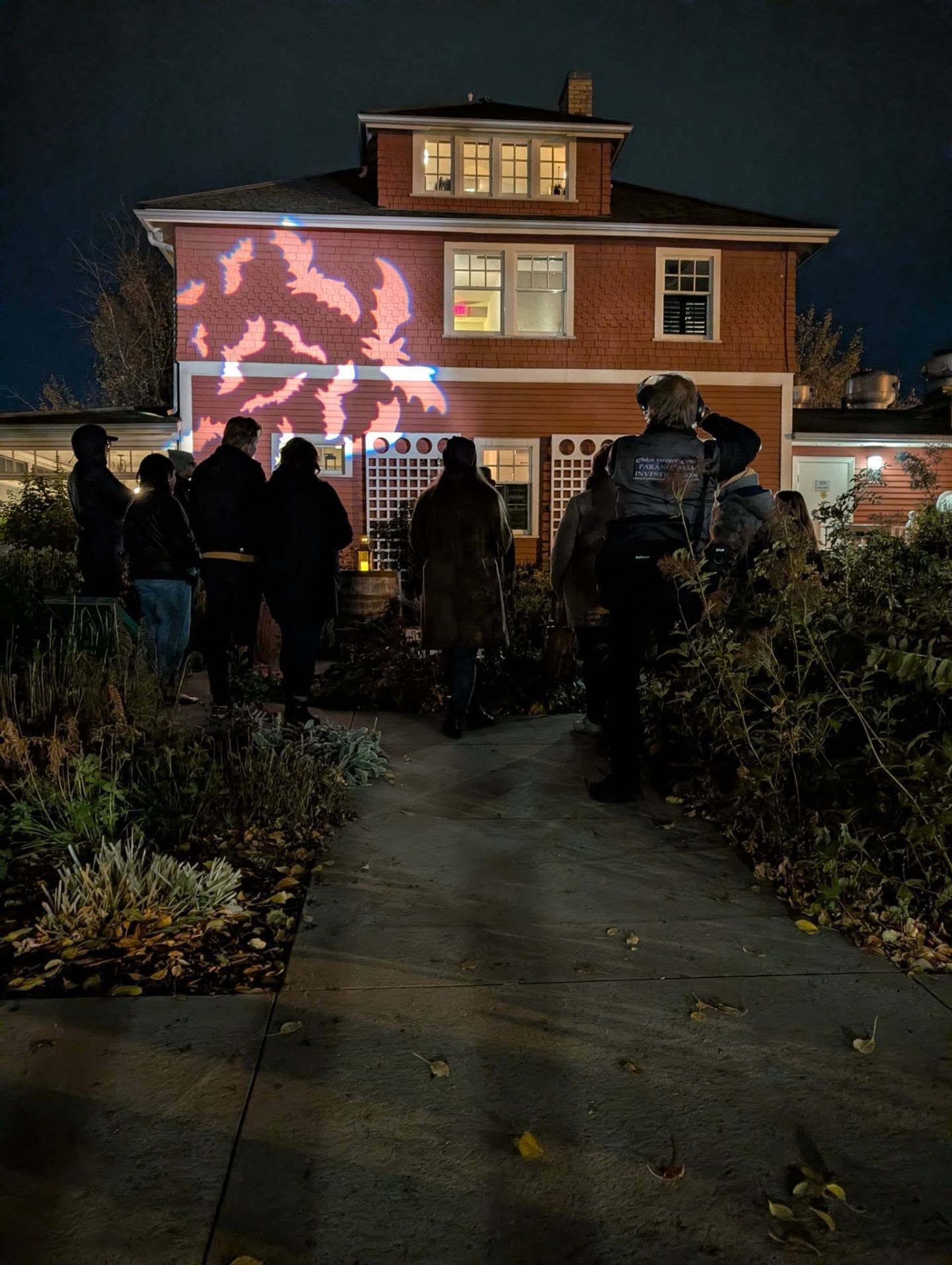 People watch colourful shapes projected onto a brick house at night.