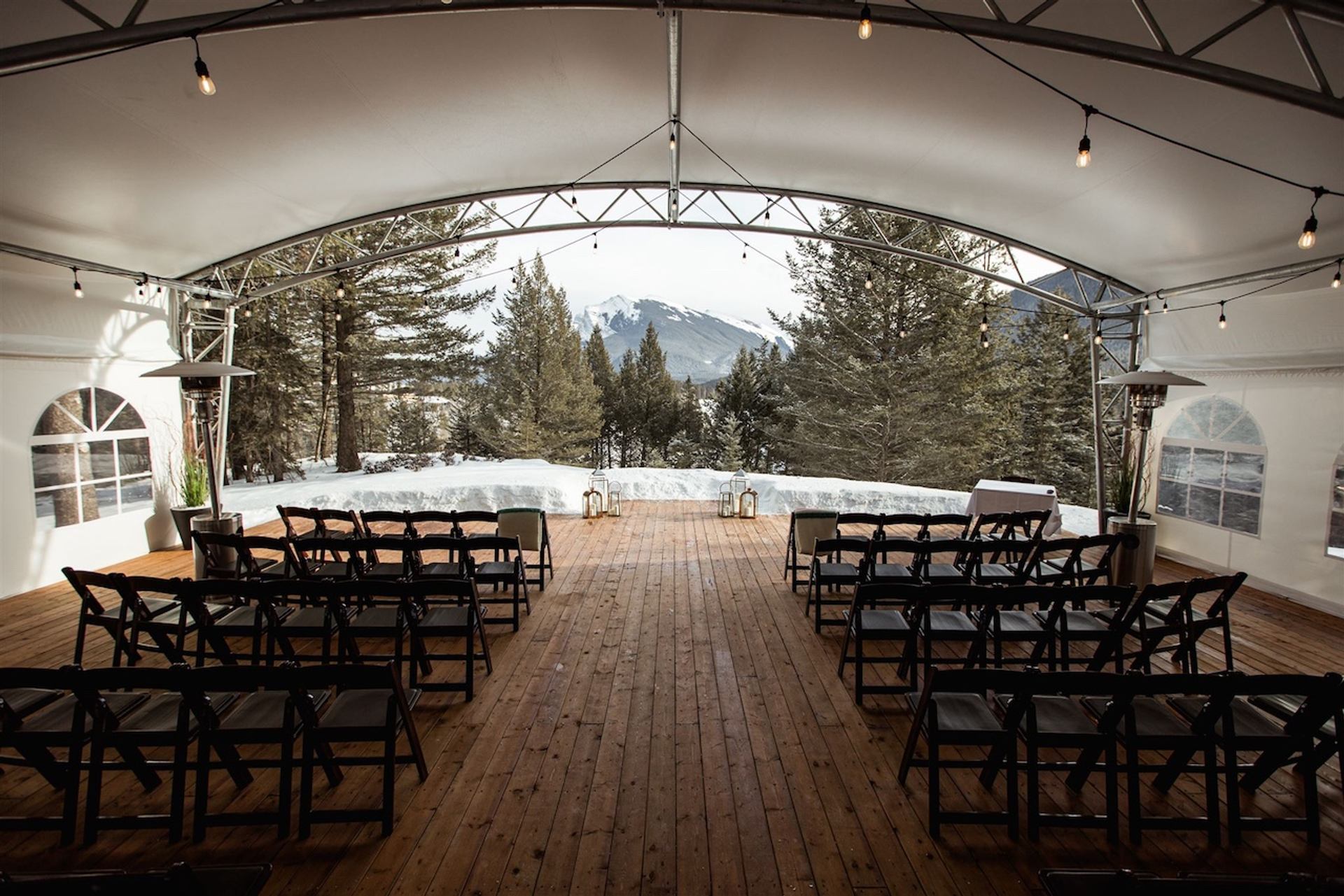 Wooden deck set with chairs under a tent facing snowy mountains