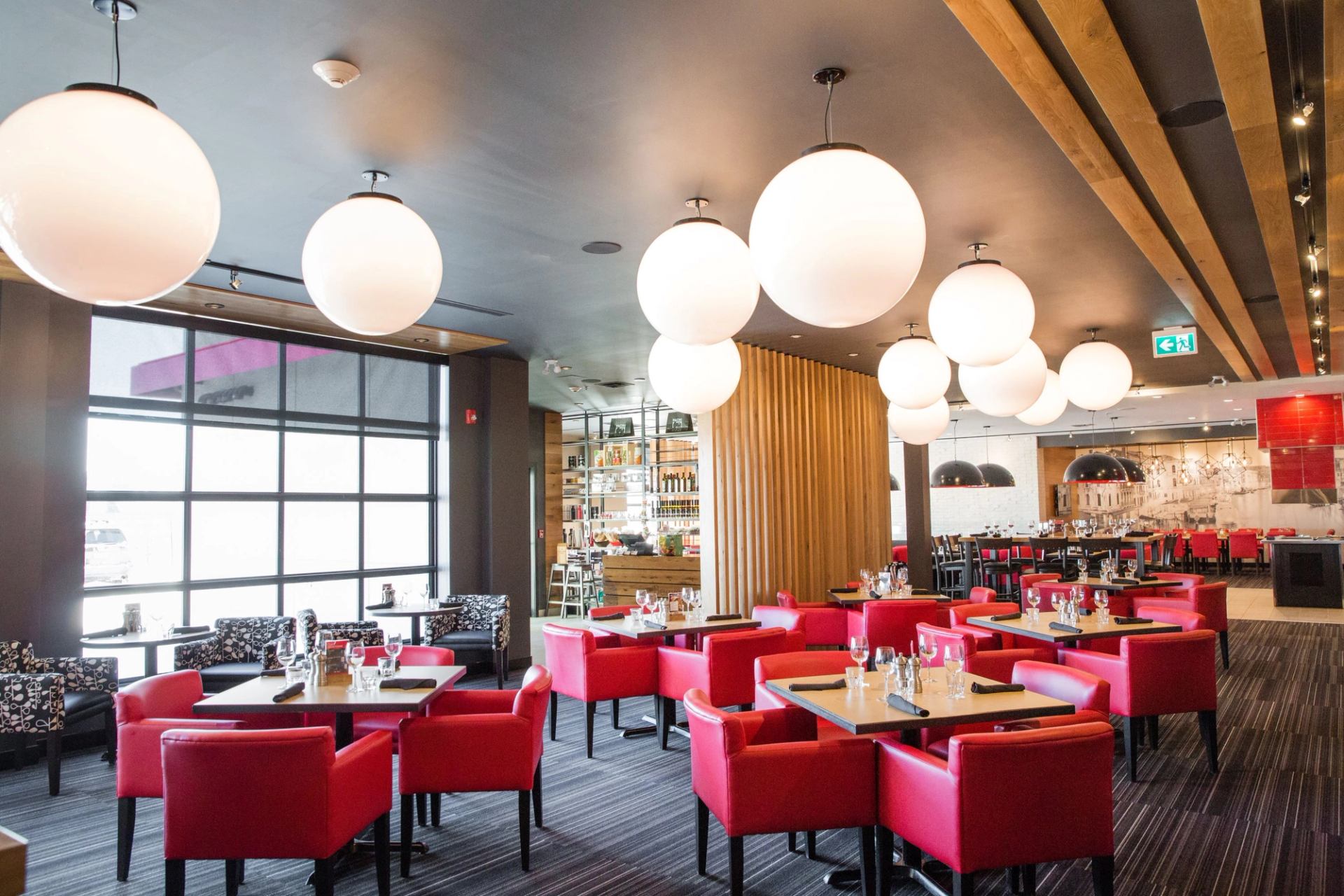 Modern restaurant with red chairs, wooden tables, and pendant lighting.