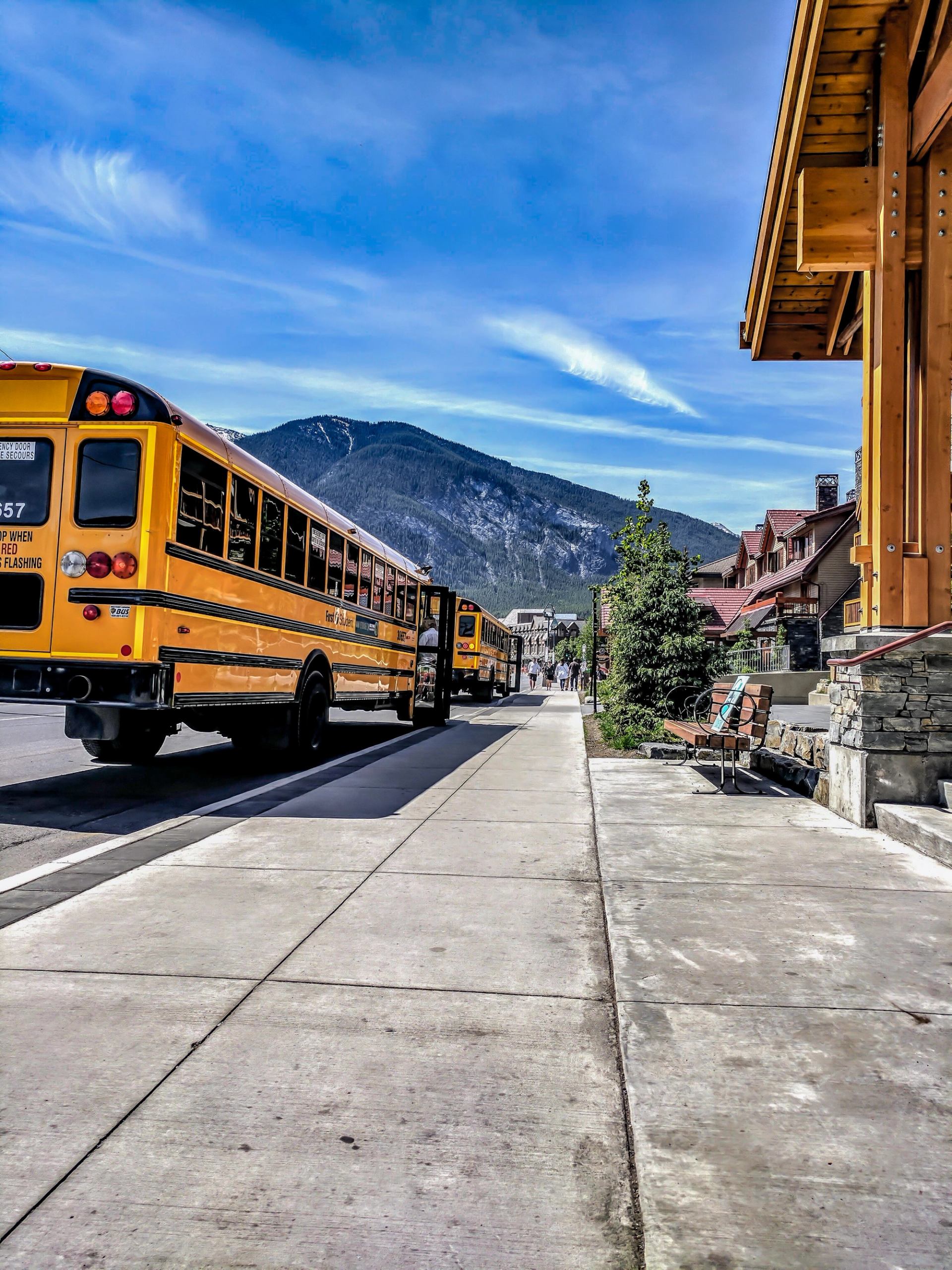 Yellow school buses parked on a street in a mountain town under a blue sky.
