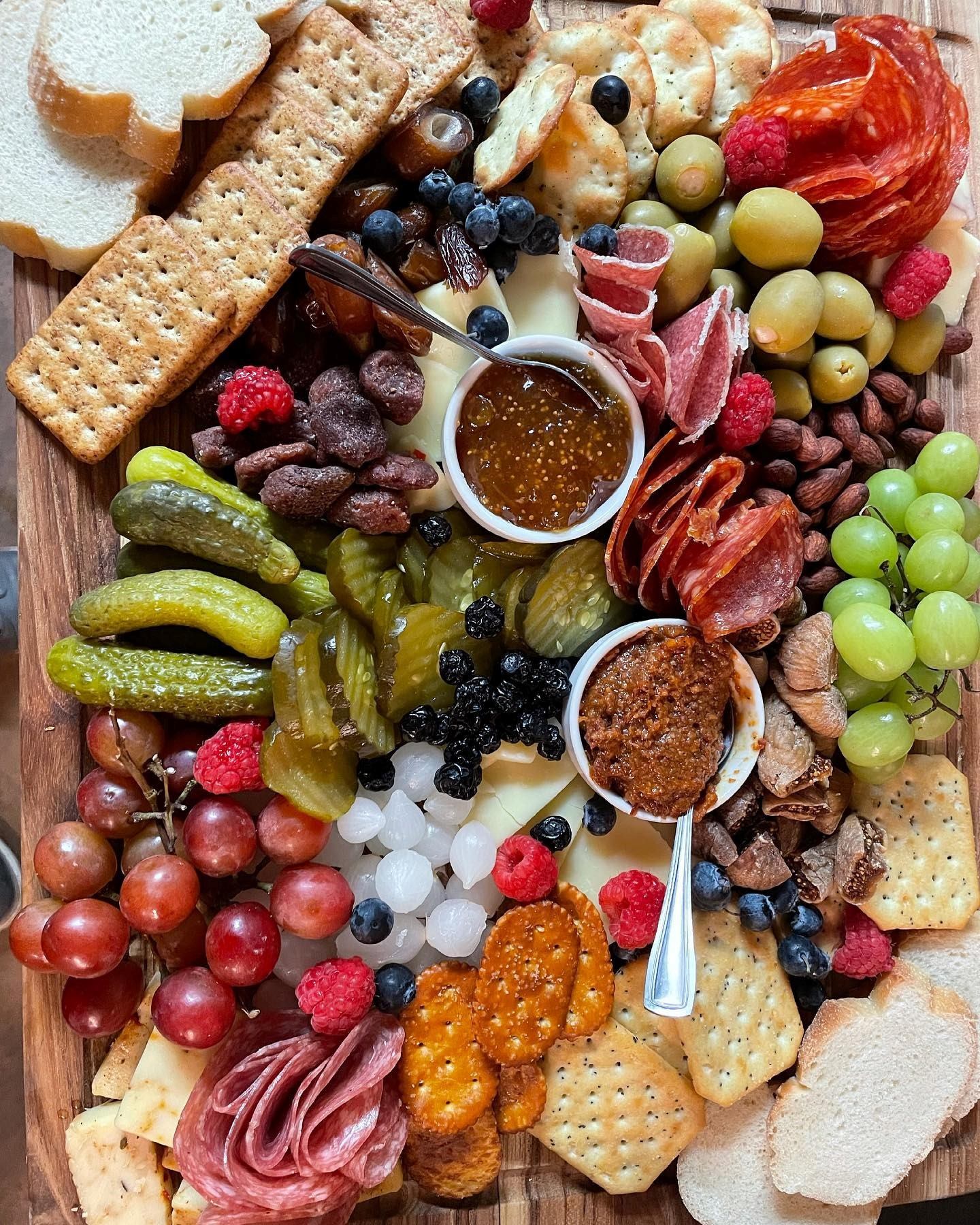 Charcuterie board with sliced meats, cheeses, olives, pickles, grapes, crackers and dips.